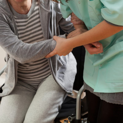 Home health care nurse helping a woman stand up from her wheelchair