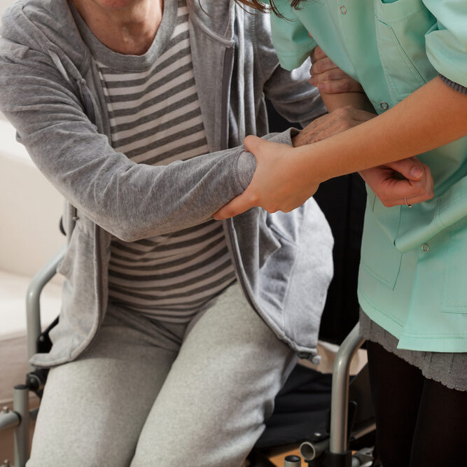Home health care nurse helping a woman stand up from her wheelchair